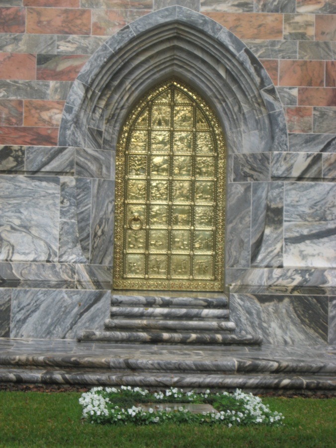 The Golden Door on the north side of the Tower, depicting the Creation and Fall of Man. Mr. Bok's grave lies at the foot of the stairs, surrounded by white flowers. 