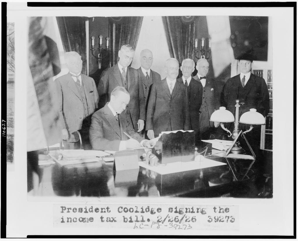The President signs the Revenue Act, 1926. To the left of the legislators stands Secretary Mellon, Director Herbert M. Lord and Everett Sanders, all the right of the photo. Courtesy of the Library of Congress. 