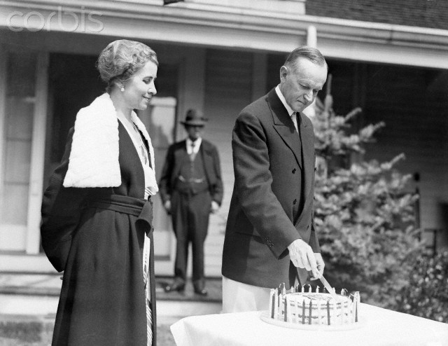Coolidge cuts the cake made for his 59th birthday, as Grace beams, at the Stearns' home in Swampscott, Massachusetts, July 1931. 